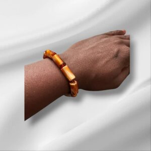 A dark-skinned wrist wearing the Irawo Beaded Bracelet made of handcrafted amber-colored beads, set against a soft white background.